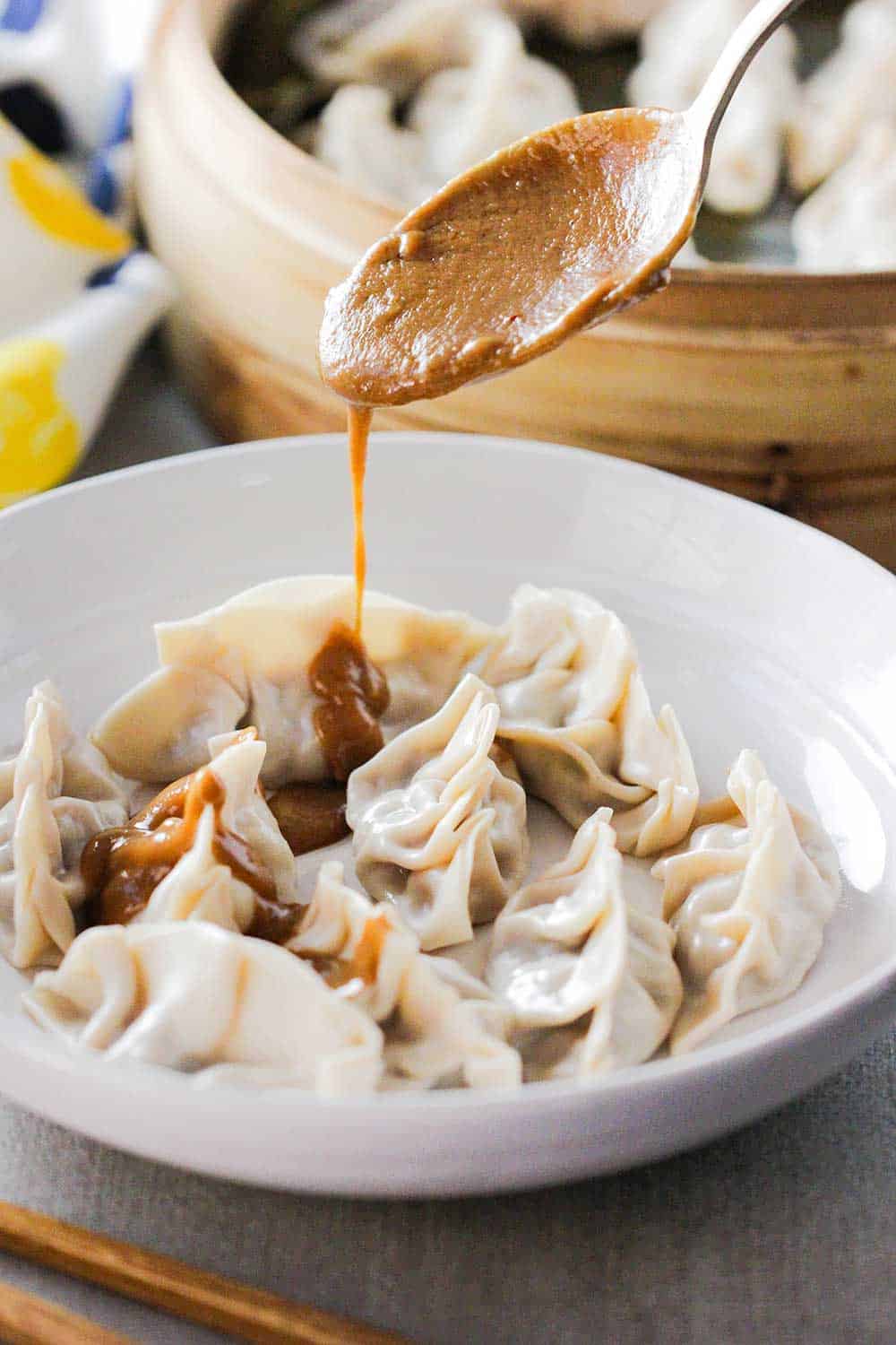 Spicy peanut sauce being poured onto steamed pork dumplings. 