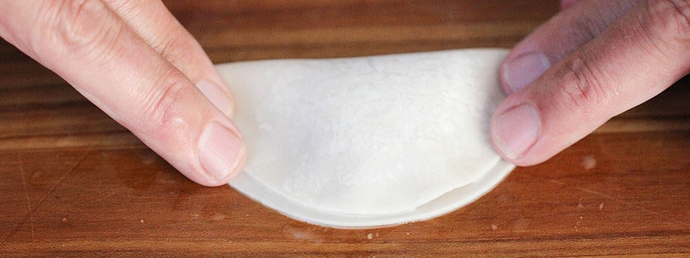 Two hands folding over the sides of a pork dumpling wrapper. 