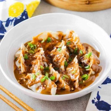 A white bowl of pork dumplings with spicy peanut sauce.