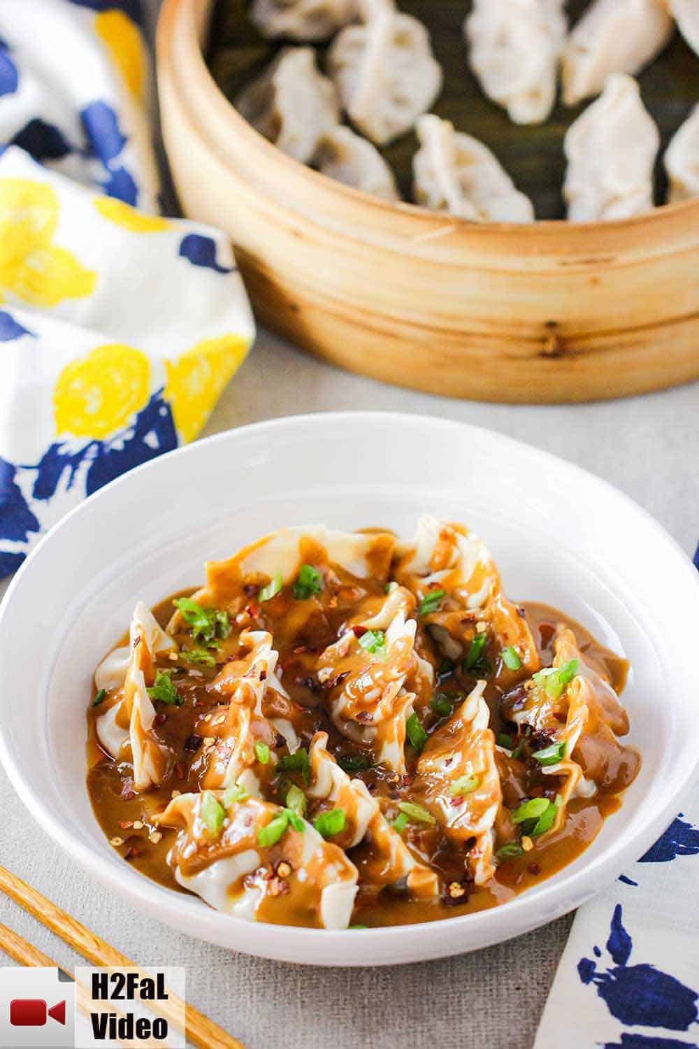 A white bowl of steamed pork dumplings with a spicy peanut sauce over the top. 