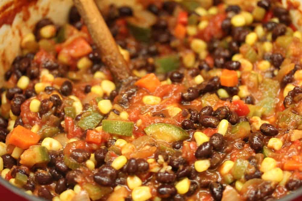 A wooden spoon stuck into a large pot of vegetarian black bean chili 