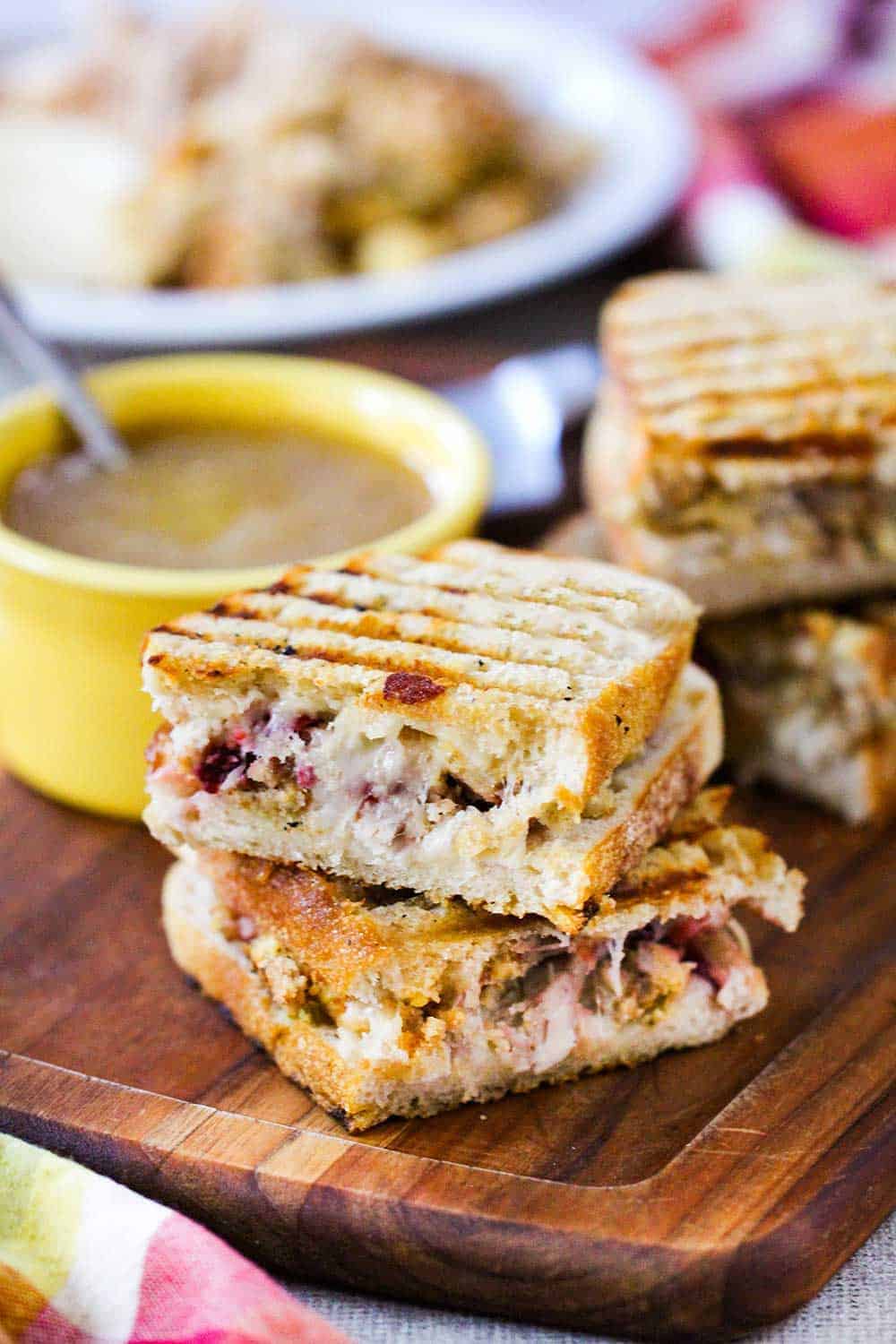 A day after Thanksgiving panini that has been cut in half and stack on a cutting board next to a bowl of gravy. 