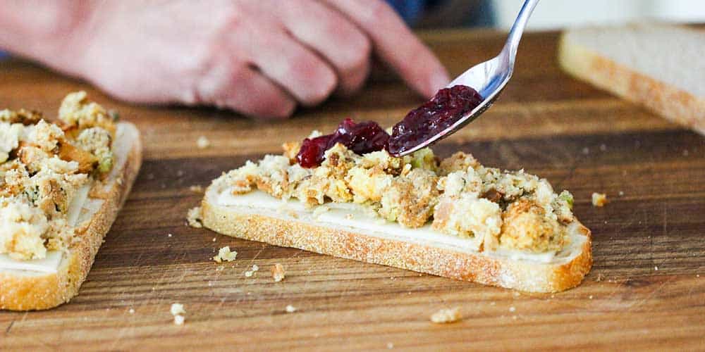 A fork adding a layer of cranberry sauce onto dressing on a sandwich. 