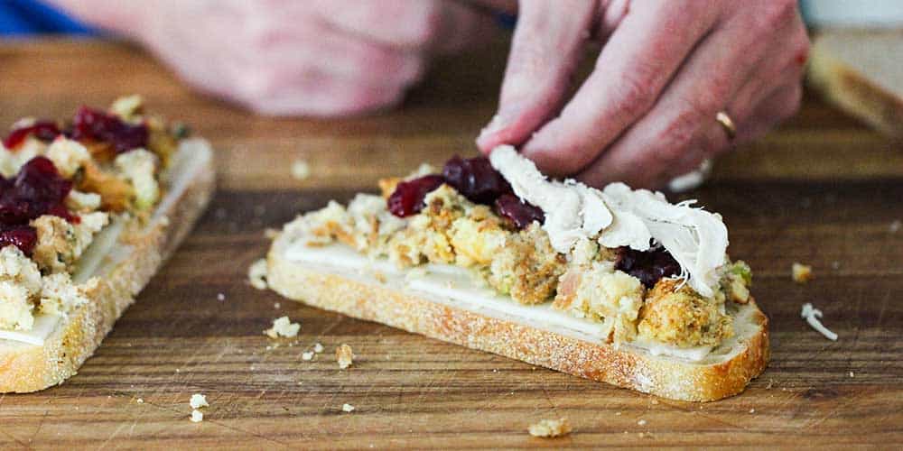 A hand adding turkey onto a day after Thanksgiving panini. 