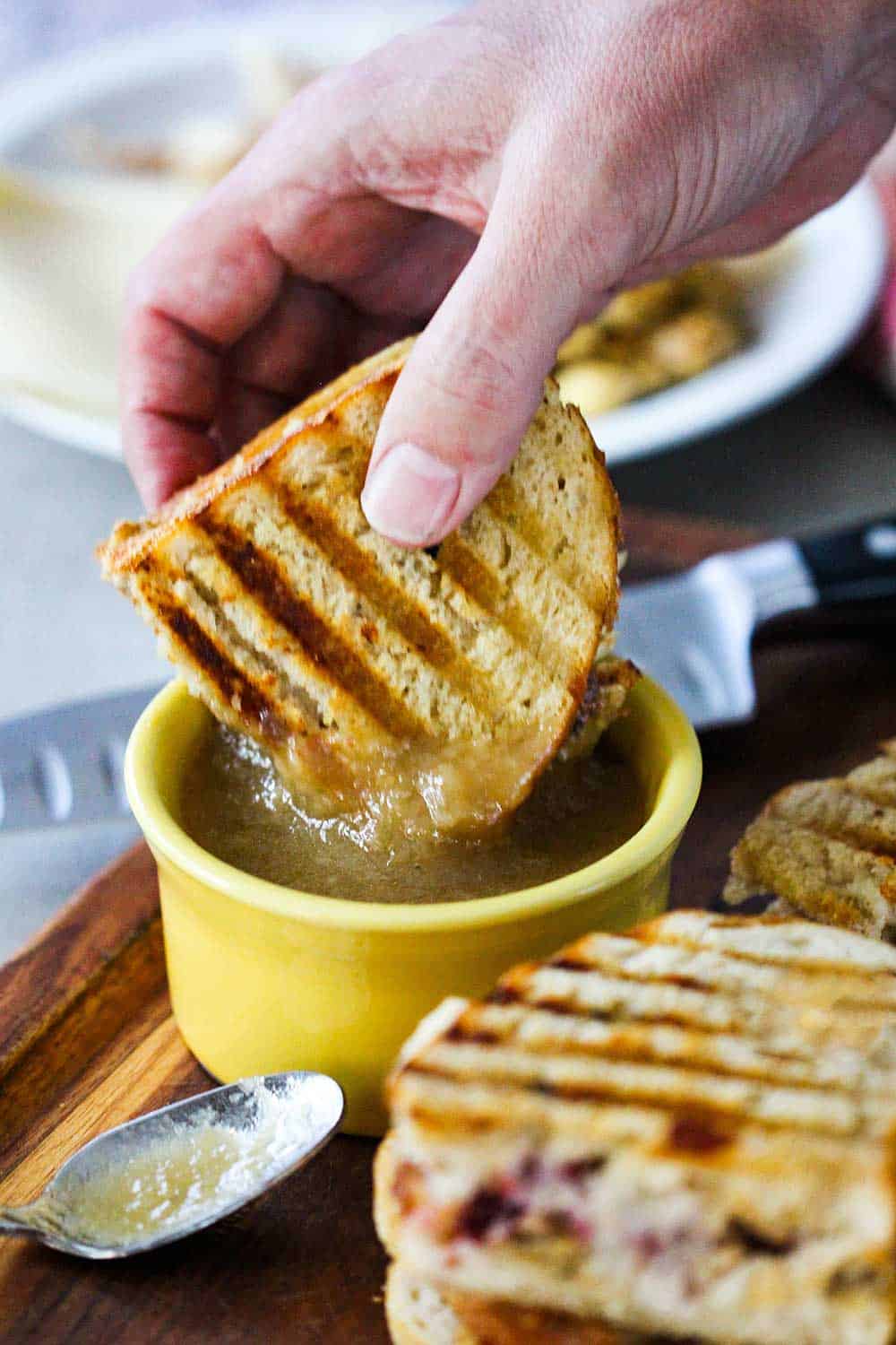 A hand dipping a Day After Thanksgiving Panini into a bowl of gravy.