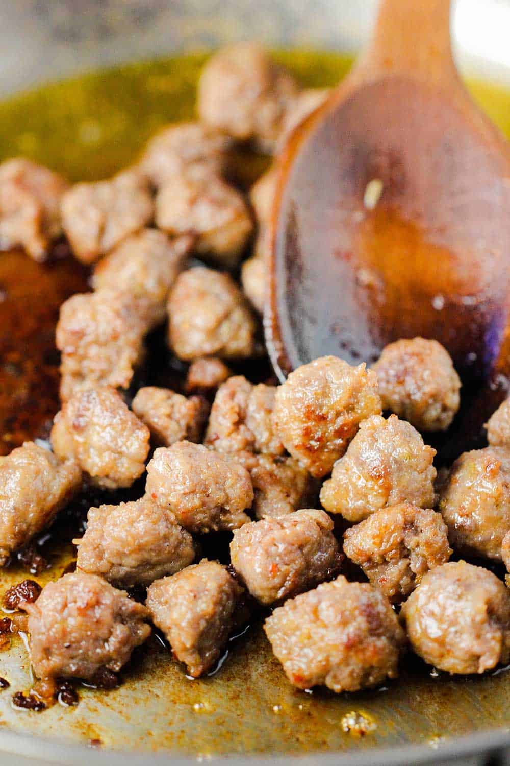 A large steel skillet with cooked Italian sausage balls in it with a wooden spoon. 