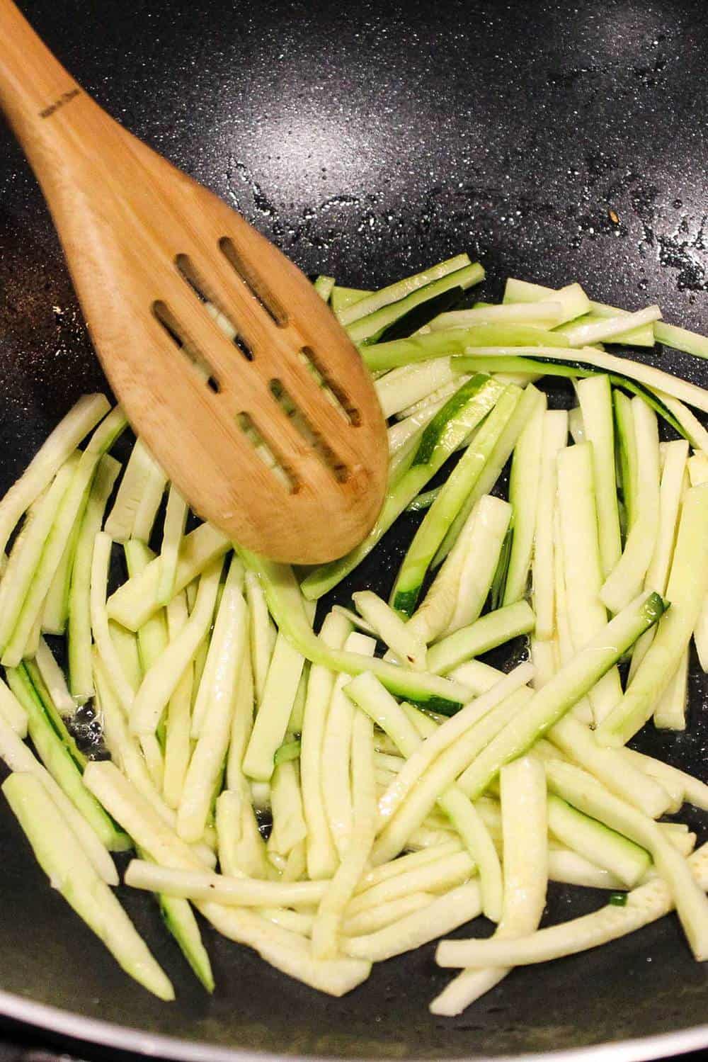 Shredded zucchini being stir fried in a wok for bibimbap