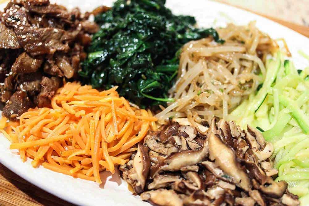 Stir fried vegetables and steak on a platter for bibimbap