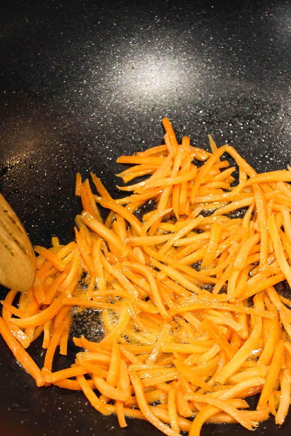 Shredded carrots being stir fried in a wok for bibimbap