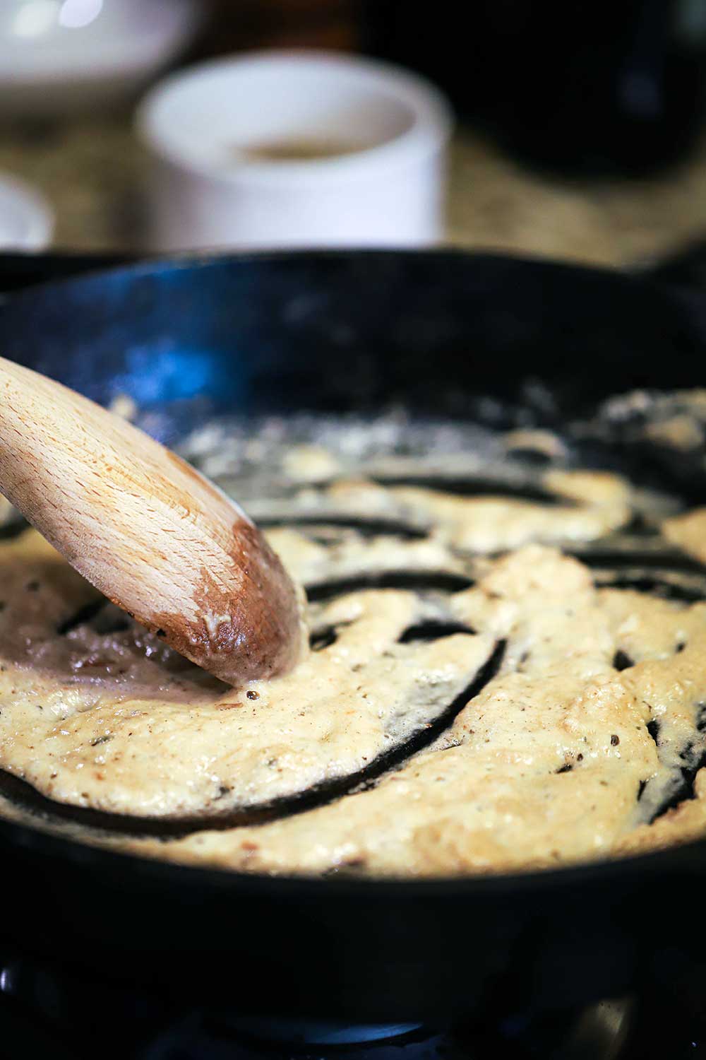 A wooden spoon stirring a blonde roux in a large black cast-iron skillet. 