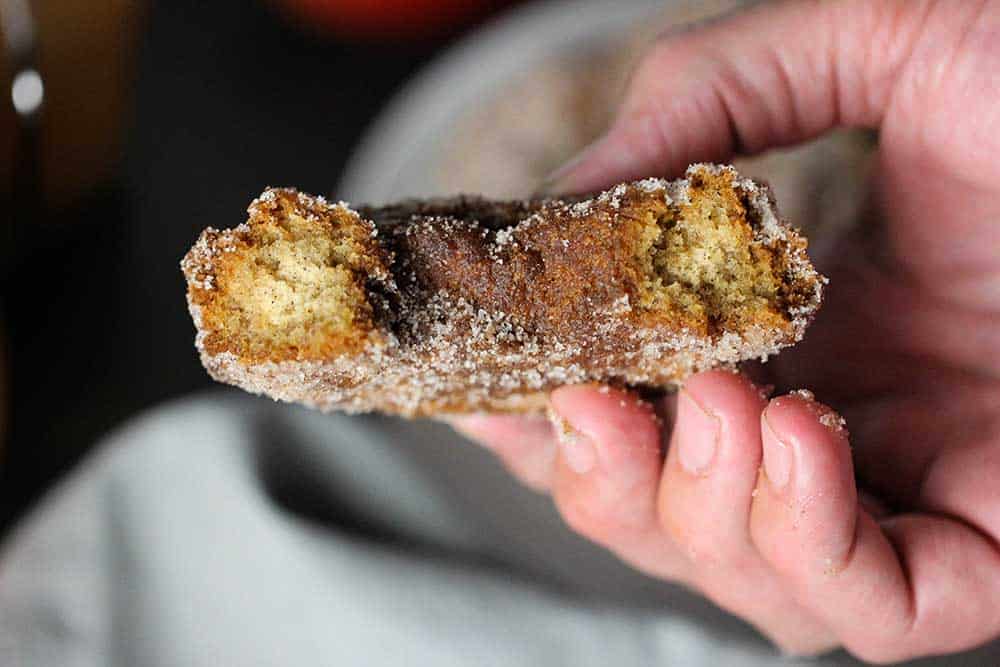 A hand holding an apple cider doughnut that has been split in half. 