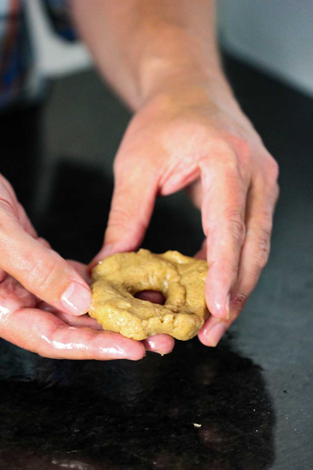 Two hands holding a doughnut shaped piece of batter for apple cider doughnuts. 