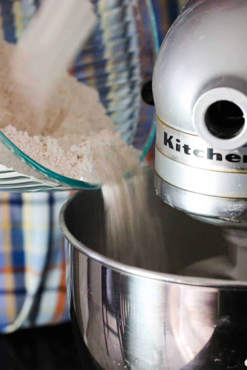 A bowl of flour and cinnamon being poured from into a large stand mixer for apple cider doughnuts. 