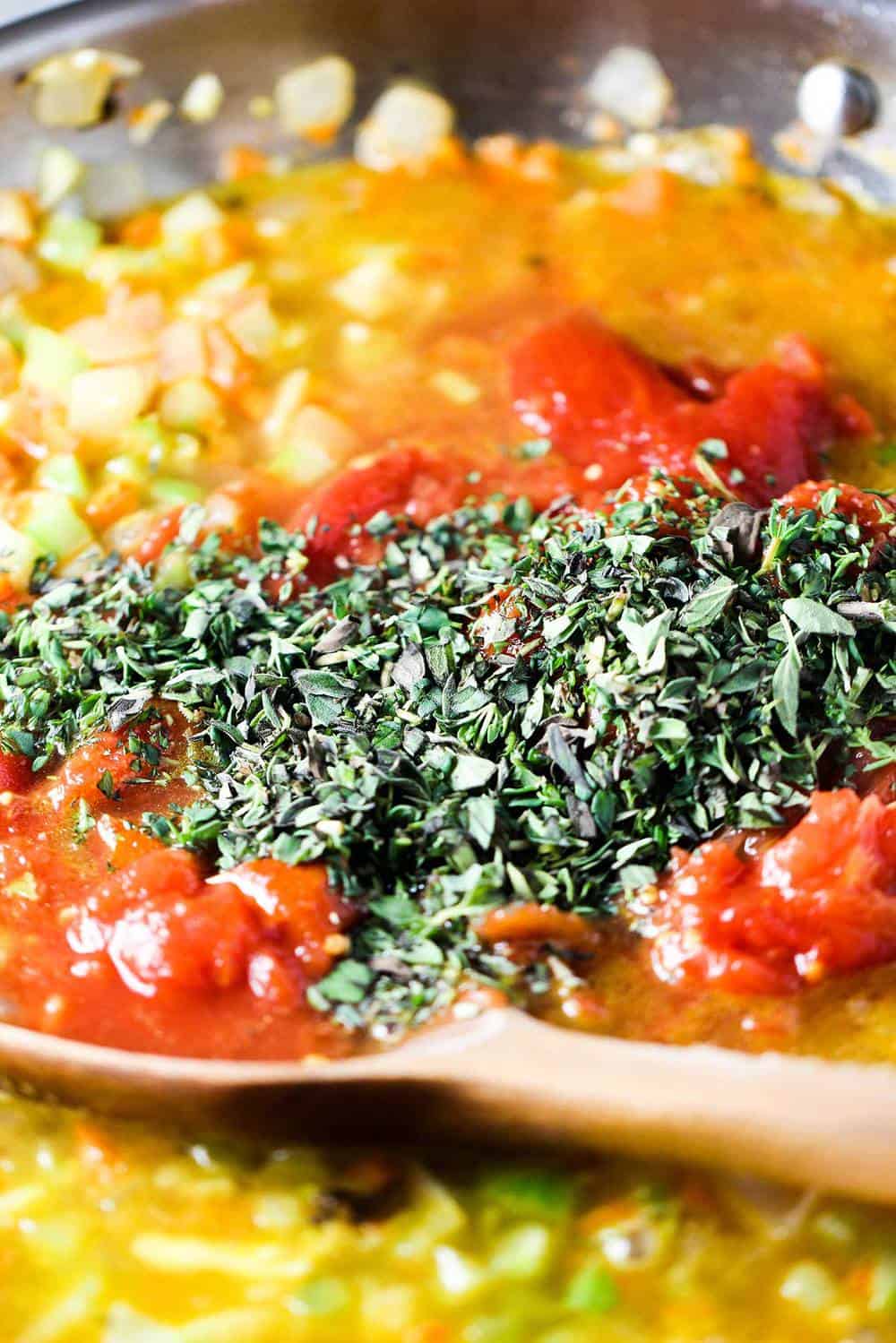 A skillet filled with sautéed vegetables and fresh herbs with a wooden spoon.