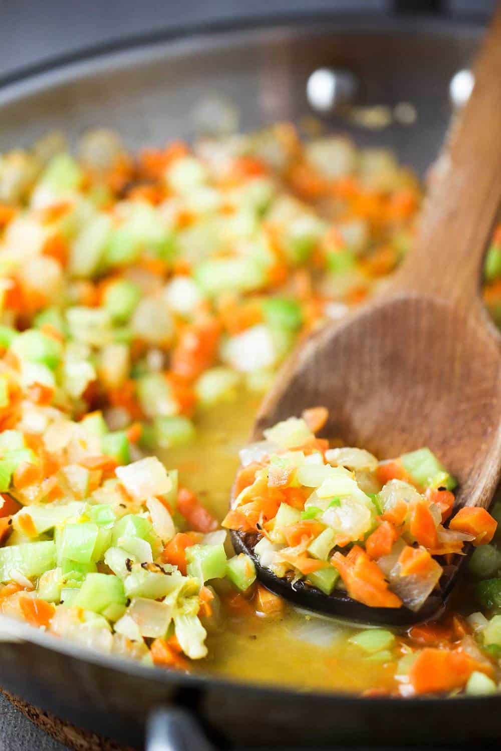Carrots, onions and celery sautéing in a skillet with a wooden spoon