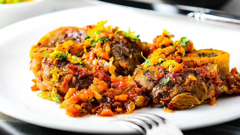 A white plate of osso buco with citrus gremolata on top. 