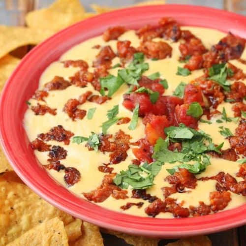 Queso with Chorizo in a red bowl next to tortilla chips