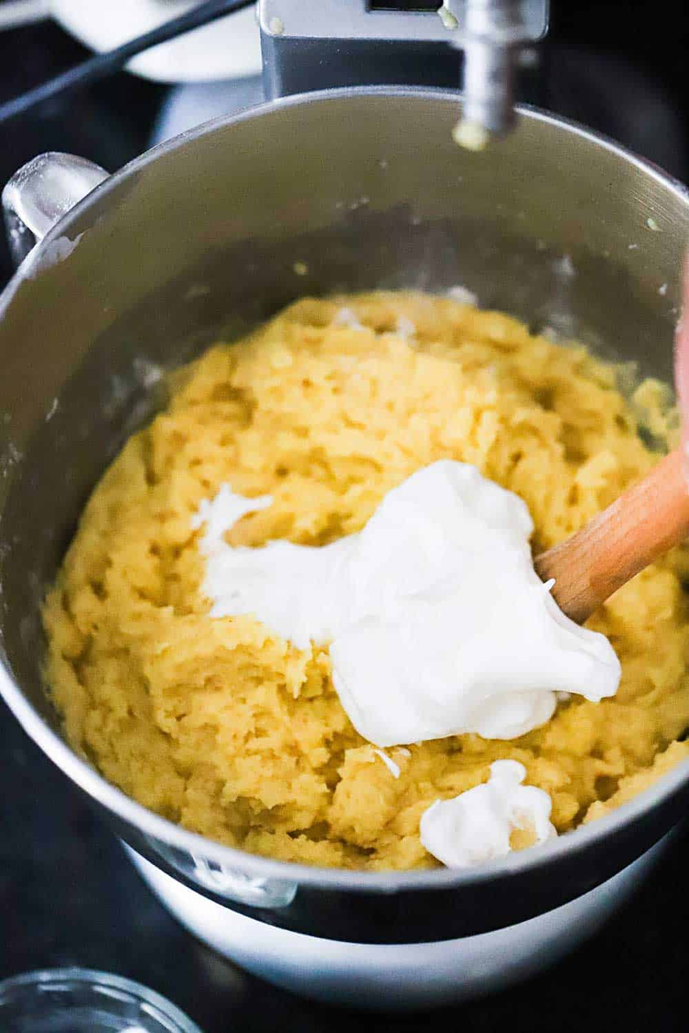 Soft peak egg whites being folded into a yellow cake batter in a metal mixing bowl. 