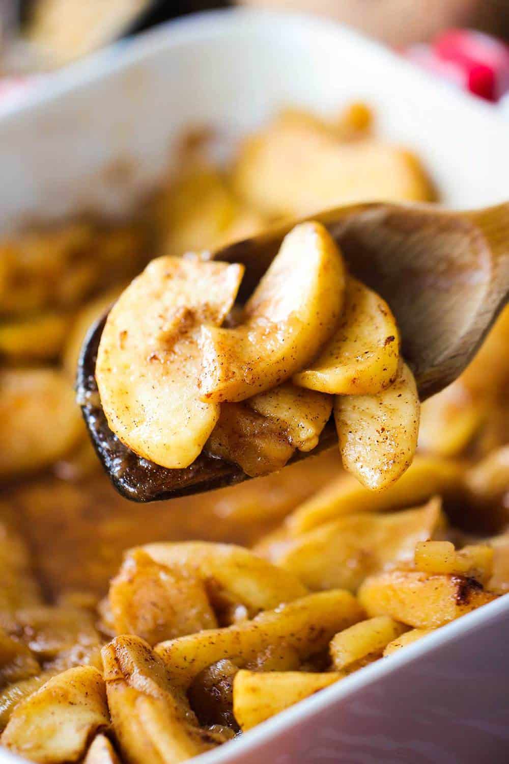 A wooden spoon holding baked cinnamon apples