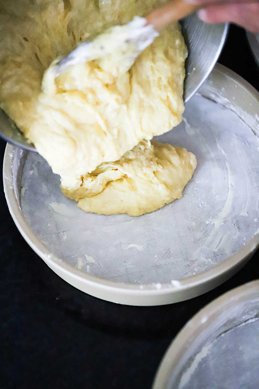 Yellow cake batter being poured into a straight-edge cake pan that has been greased and floured. 