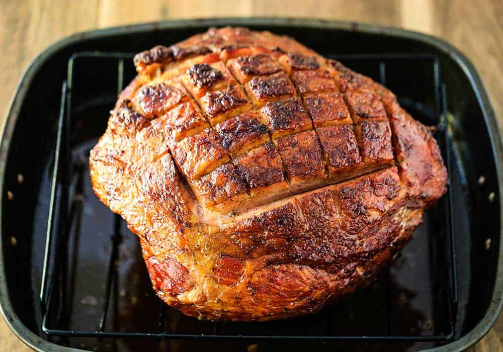 A cooked honey bourbon-roasted ham in a roasting pan on a roasting rack. 