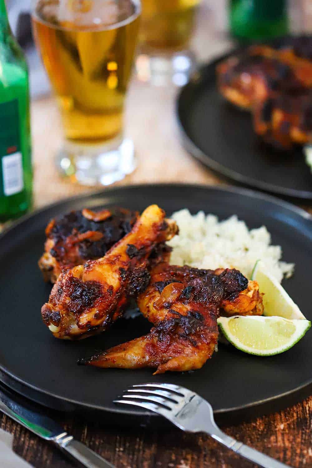 A black dinner plate filled with two pieces of roasted chipotle chicken, cilantro-lime rice, and 2 lime wedges, all sitting next to a glass of Mexican beer.