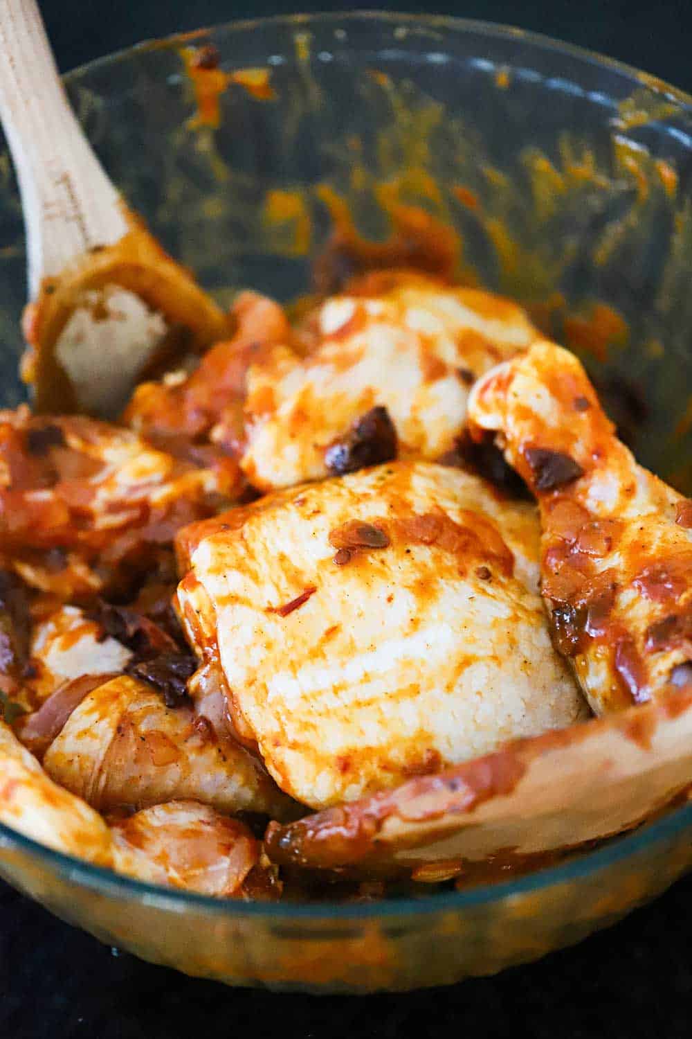 A large glass bowl filled with skin-on chicken pieces that have been coated with a chipotle BBQ sauce. 