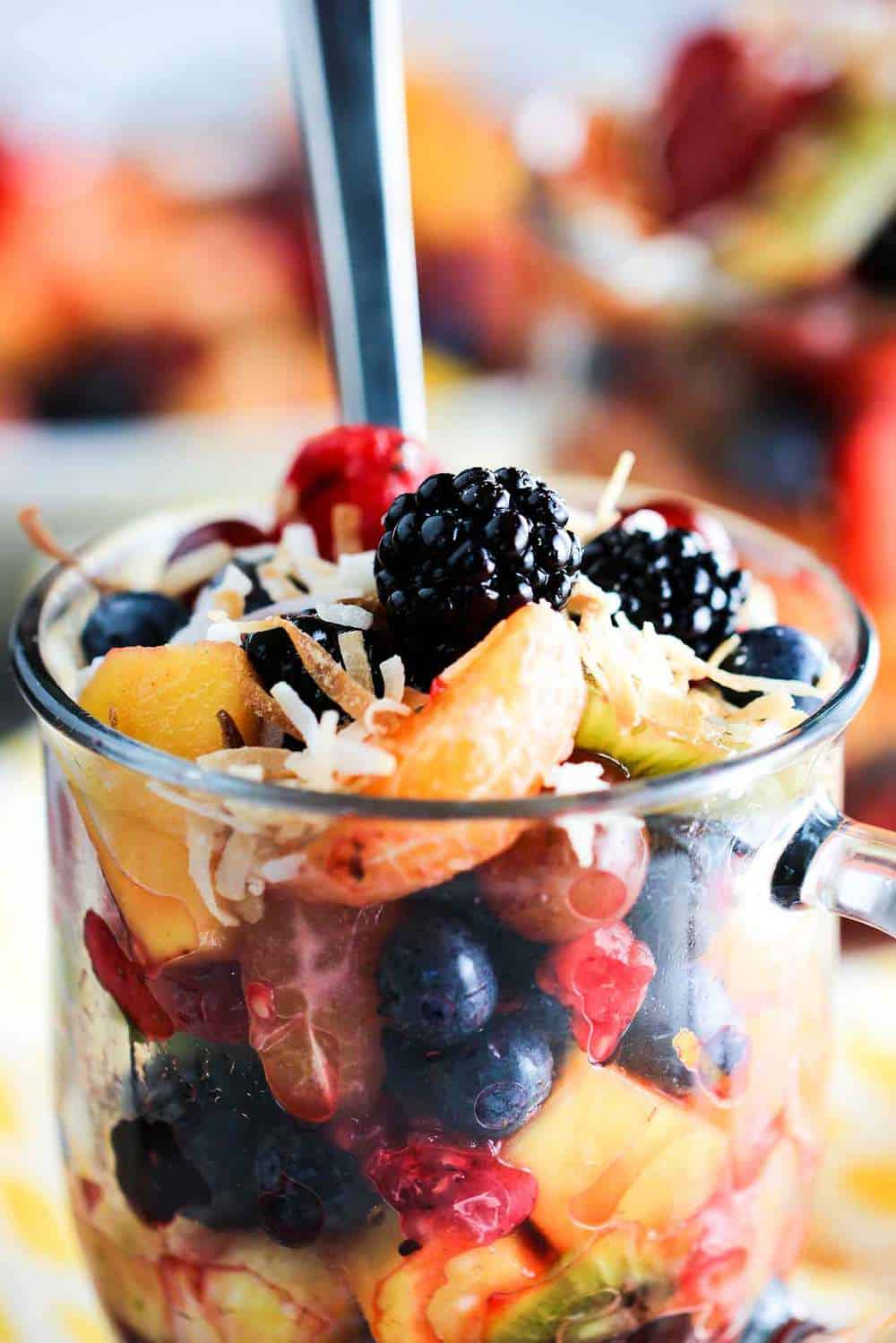 A large glass of summer fruit salad with a fork stuck in it.