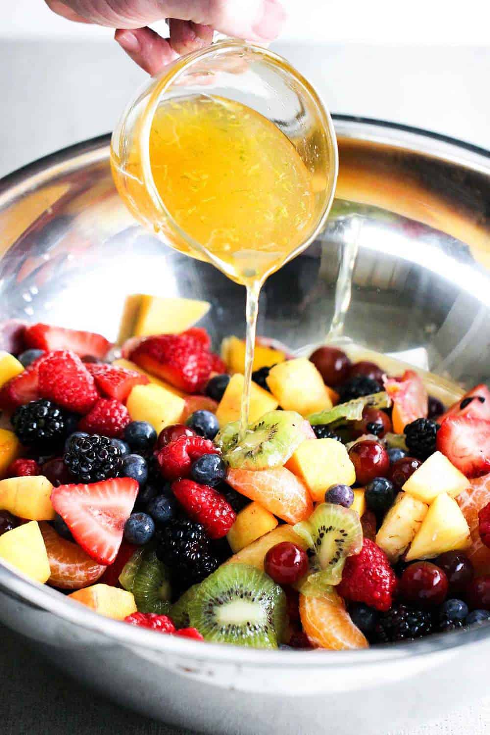 Dressing pouring onto a bowl of fruit for summer fruit salad. 