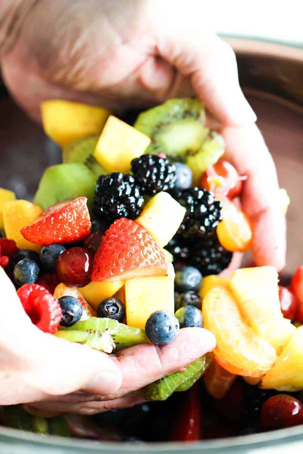 Two hands holding an assortment of berries and fruit for summer fruit salad