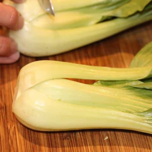 A hand cutting the tough white ends off the baby bok choy