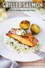 A grilled salmon fillet sitting on top of a bed of cilantro rice with poblano compound butter melting on top of the dish with two grilled limes halves nearby.