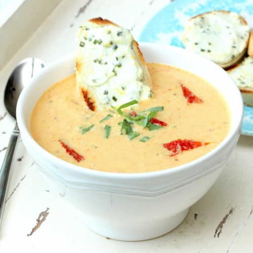 A bowl of chilled corn soup with sun-dried tomatoes on a white board.