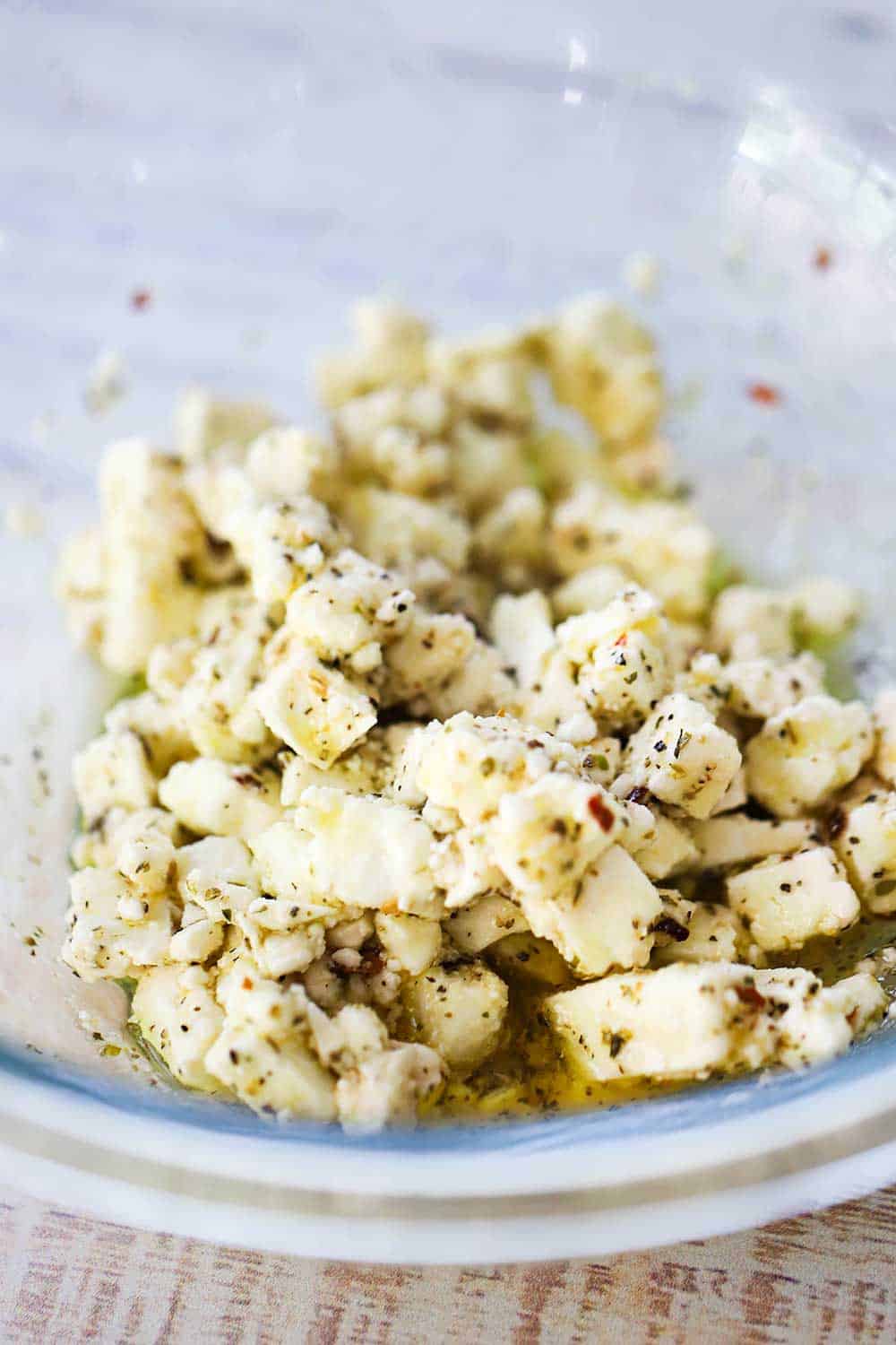 A glass bowl filled with crumbled marinated feta cheese. 