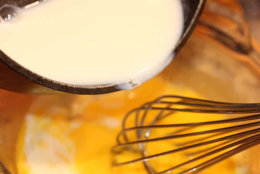 Temper the eggs by pouring in the warm cream with a whisk