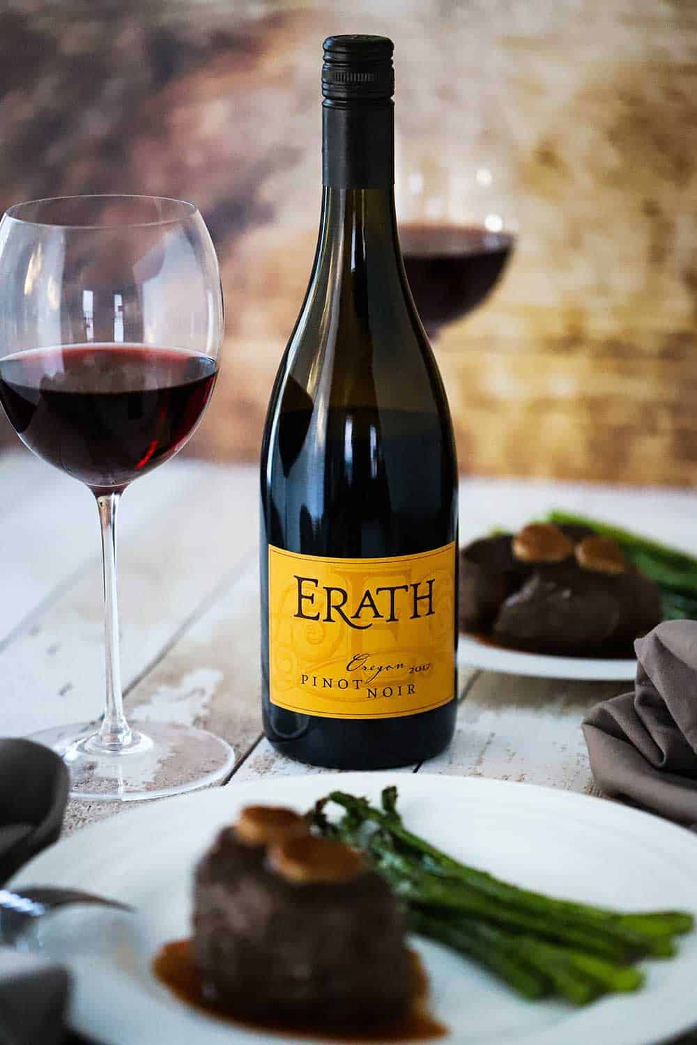 A bottle of Erath Oregon Pinot Noir sitting next to a plate of filet mignon and roasted asparagus. 