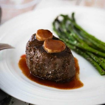 A white plate holding a filet mignon with classic Bordelaise sauce and a side of roasted asparagus.