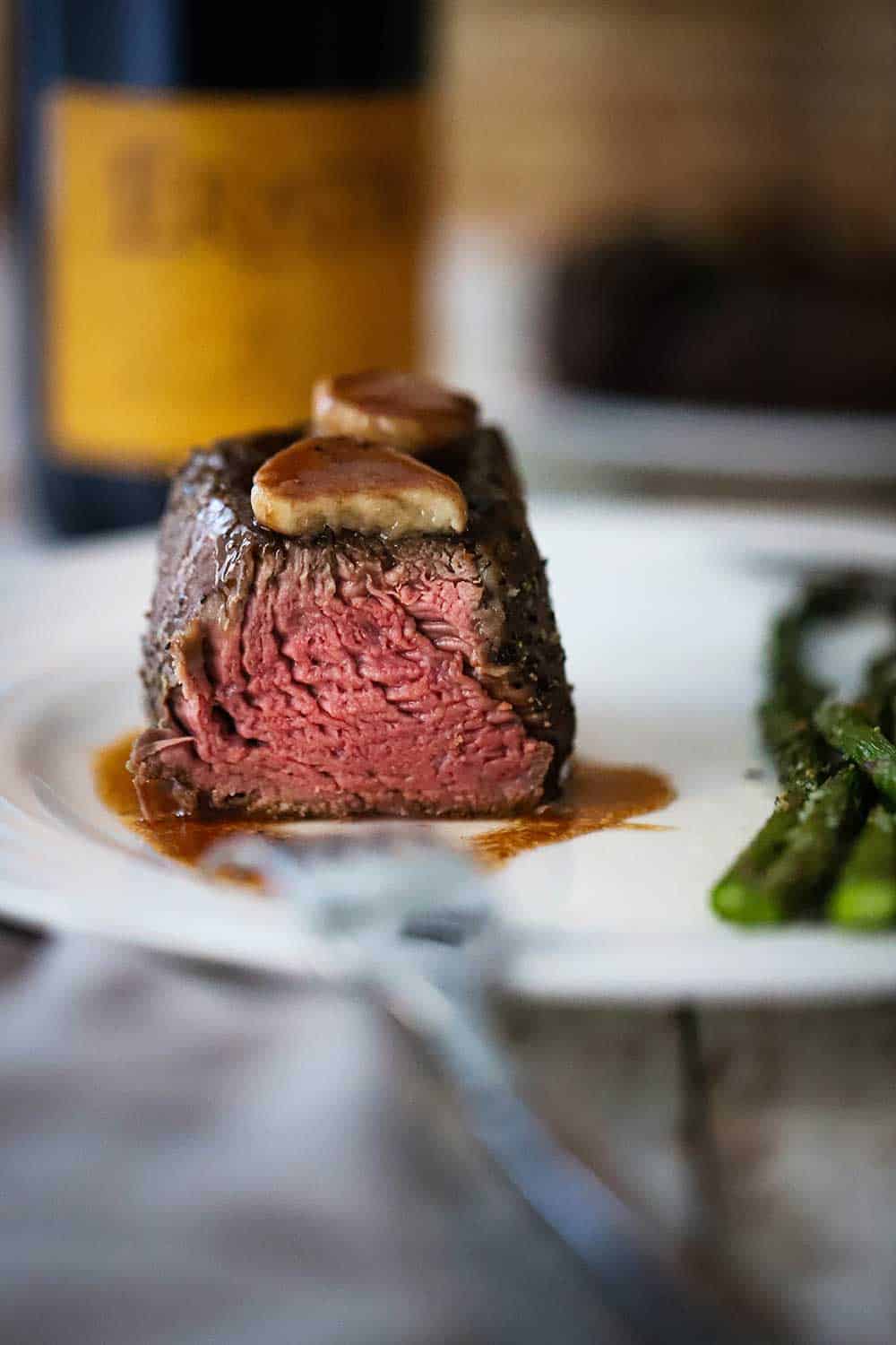 A large fillet mignon that has been sliced in half and it pink on the inside and seared on the outside with two beef bone marrow medallions on top. 