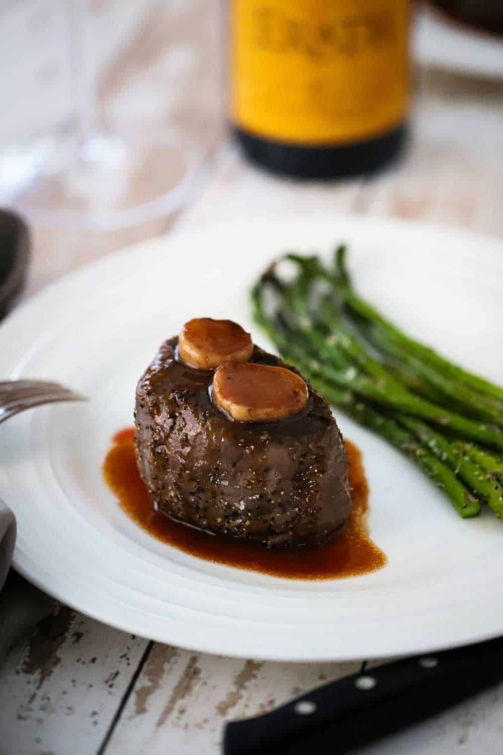 A white plate holding a filet mignon with classic Bordelaise sauce and a side of roasted asparagus.