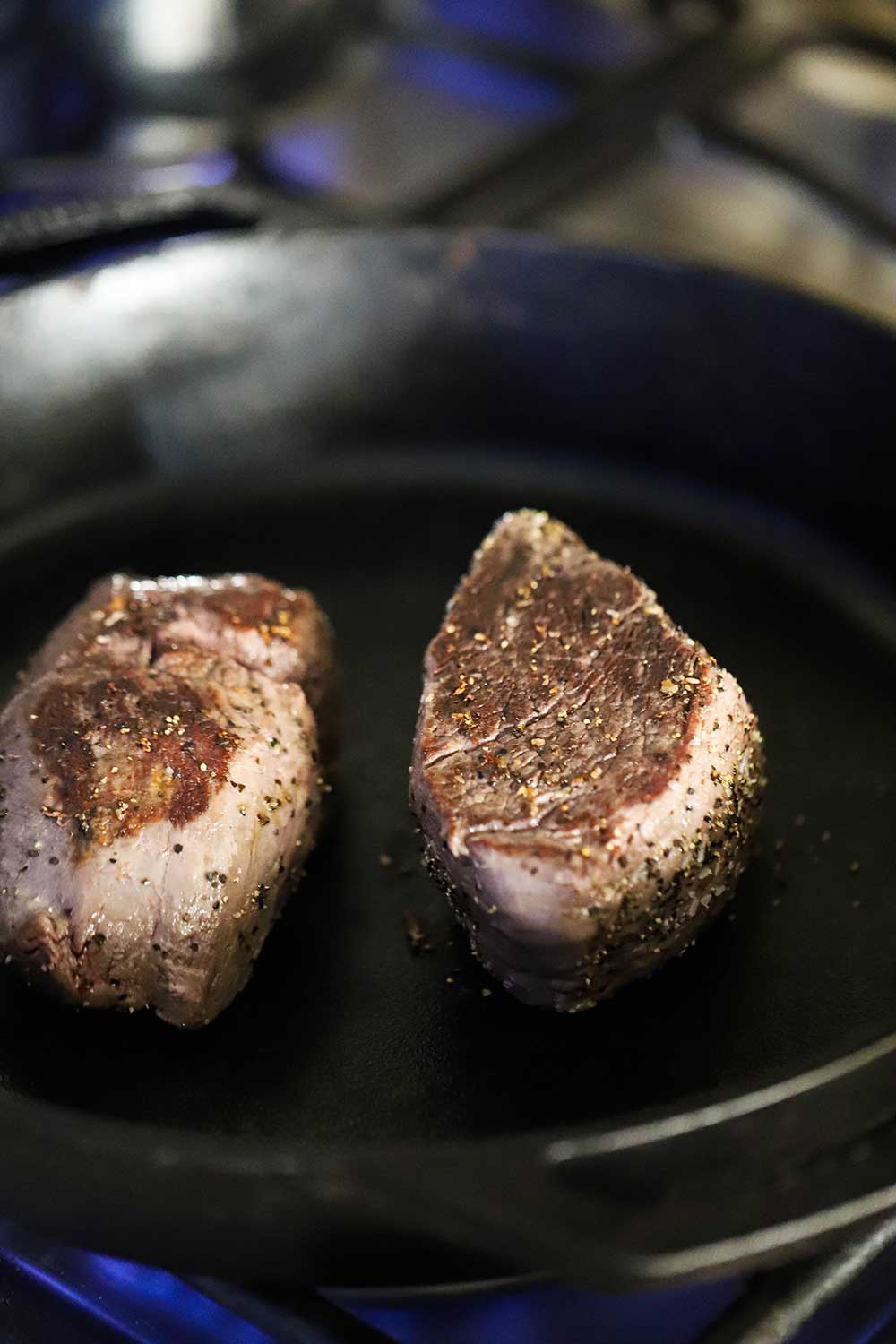 Two beef tenderloin steaks that have been seared and are sitting in a large cast-iron skillet. 