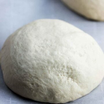 A ball of semolina pizza dough sitting on parchments paper next to another dough ball.