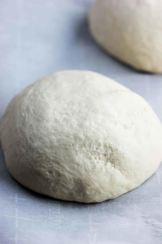 A ball of semolina pizza dough sitting on parchments paper next to another dough ball.