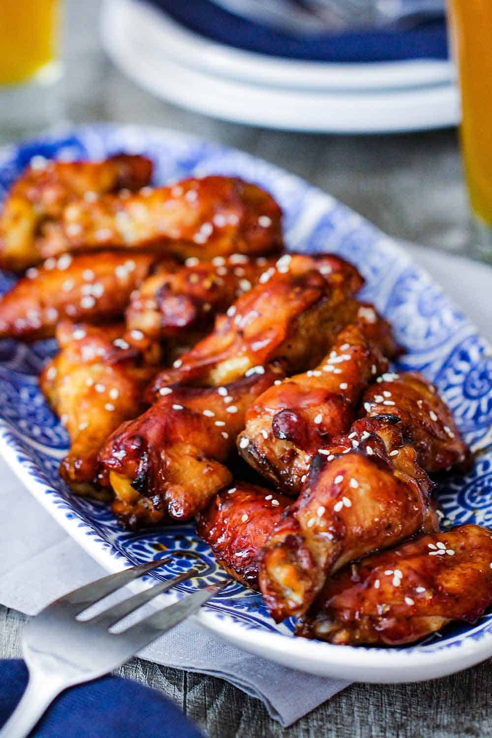 A close up view of a blue platter holding teriyaki chicken wings. 