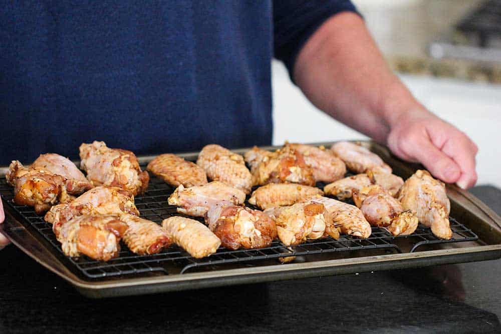 Two hands holding a baking rack on a baking sheet filled with uncooked teriyaki chicken wings. 