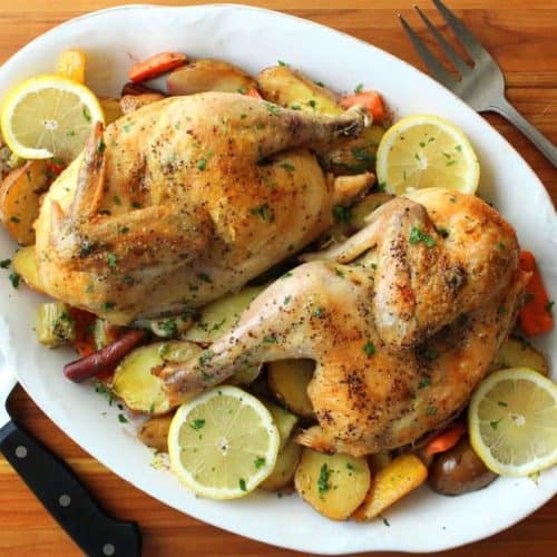 Roasted Lemon Chicken with Vegetables on a white dish next to a knife and fork