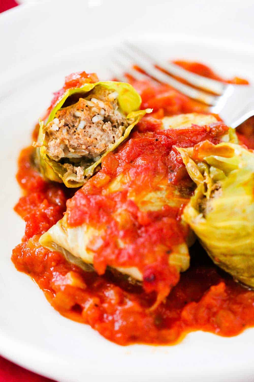 A white dinner plate filled with stuffed cabbage rolls with one split in half next to a fork. 