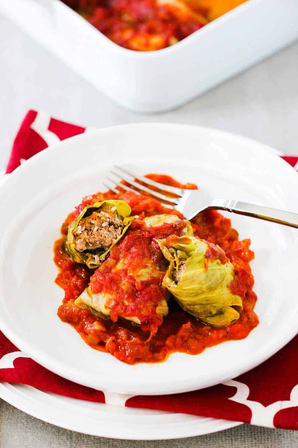 A white dinner plate filled with stuffed cabbage rolls with one split in half next to a fork. 