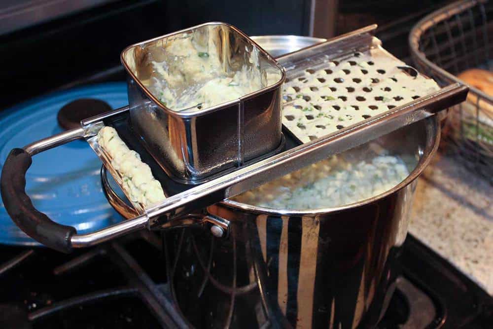 Spaetzle dough being dropped into boiling water from a spaetzle maker