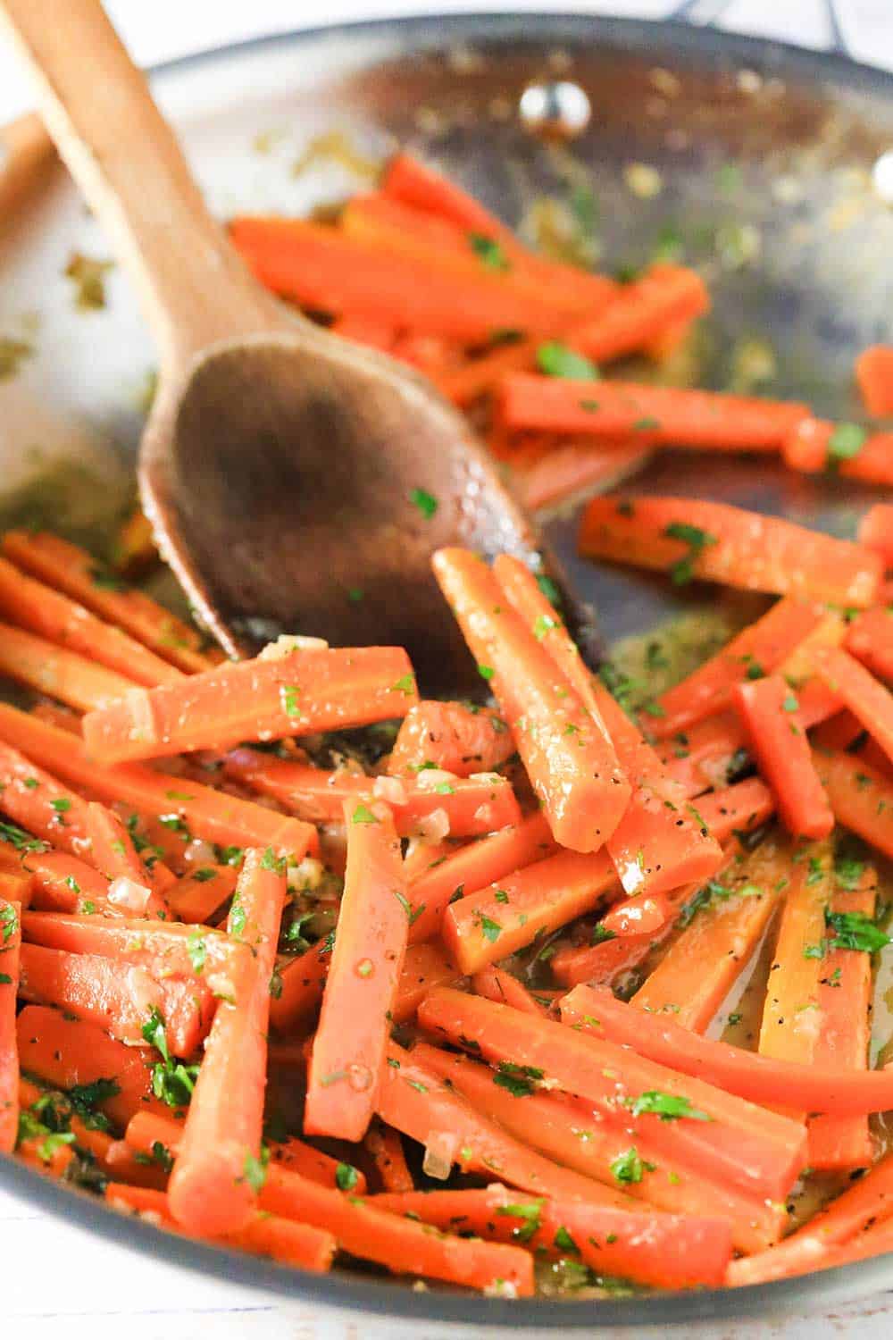 A large skillet filled with braised carrot sticks with a wooden spoon in it. 