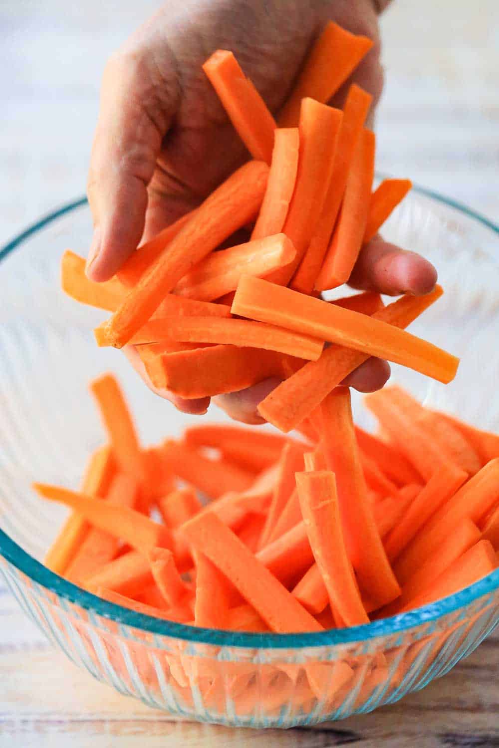 A hand dropping cut carrots into a glass bowl. 